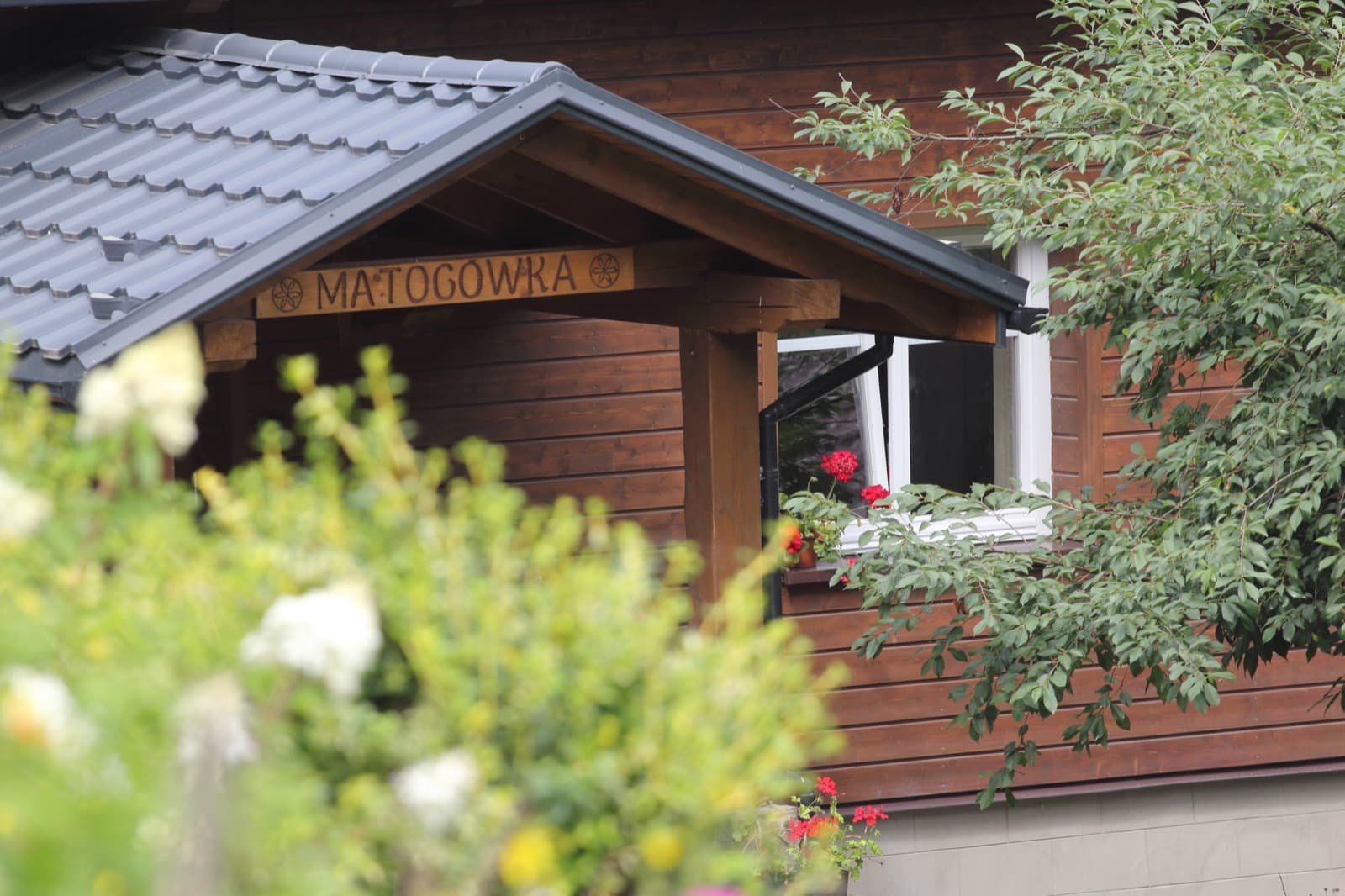 Szyld Matogówka przez zieleń ogrodu